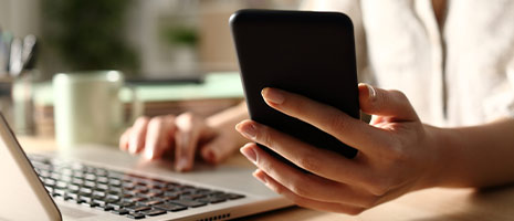 woman at laptop holding mobile